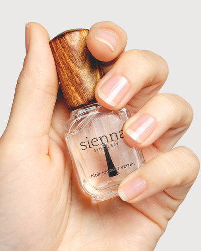 transparent base and top coat  hand swatch on fair skin tone holding a sienna bottle