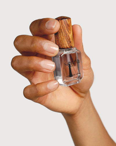 transparent base and top coat hand swatch on medium skin tone holding a sienna bottle