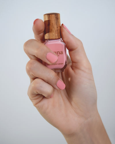 Peachy pink nail polish hand swatch on fair skin tone holding a Sienna bottle up close.