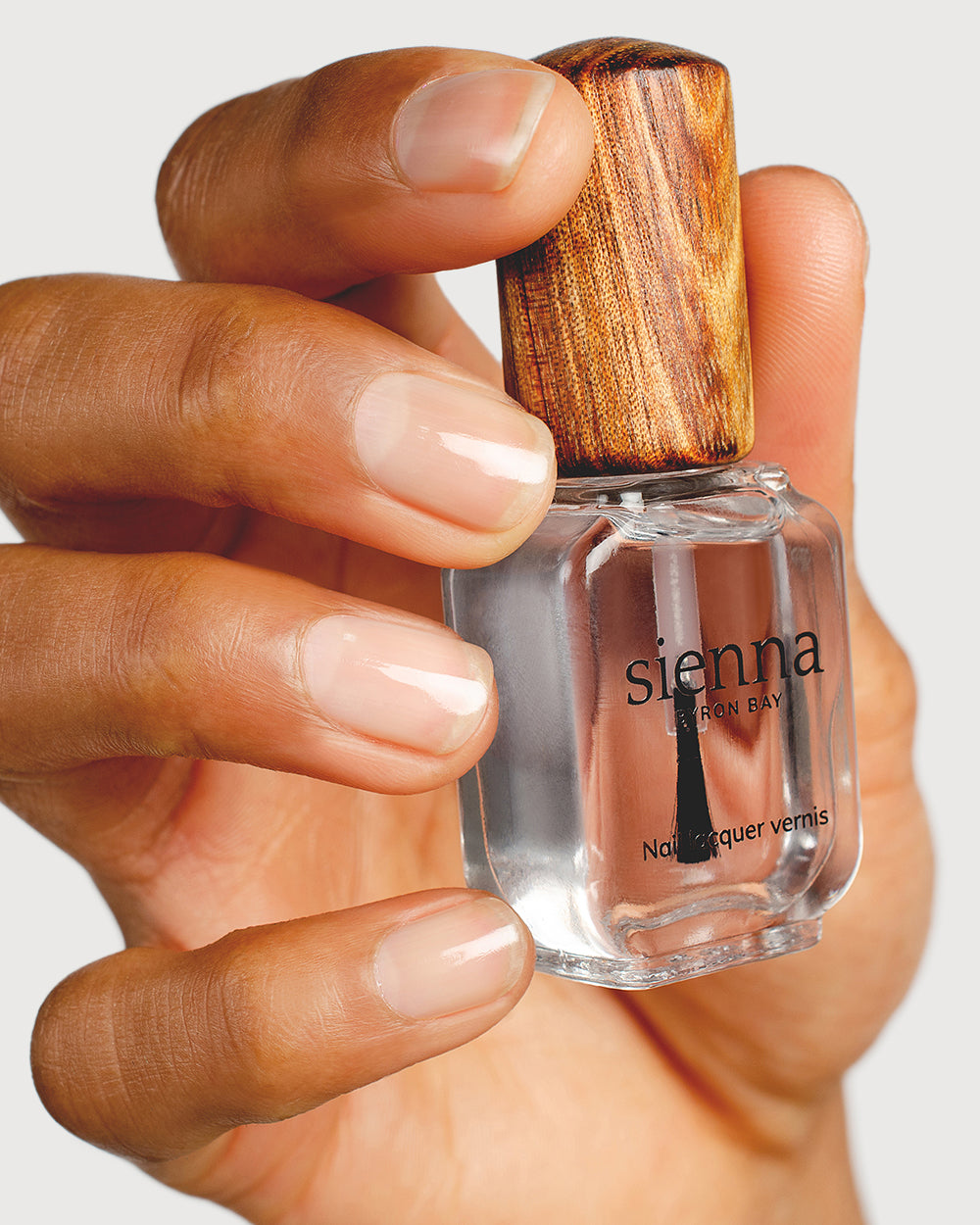 transparent base and top coat hand swatch on medium kin tone holding a sienna bottle up close